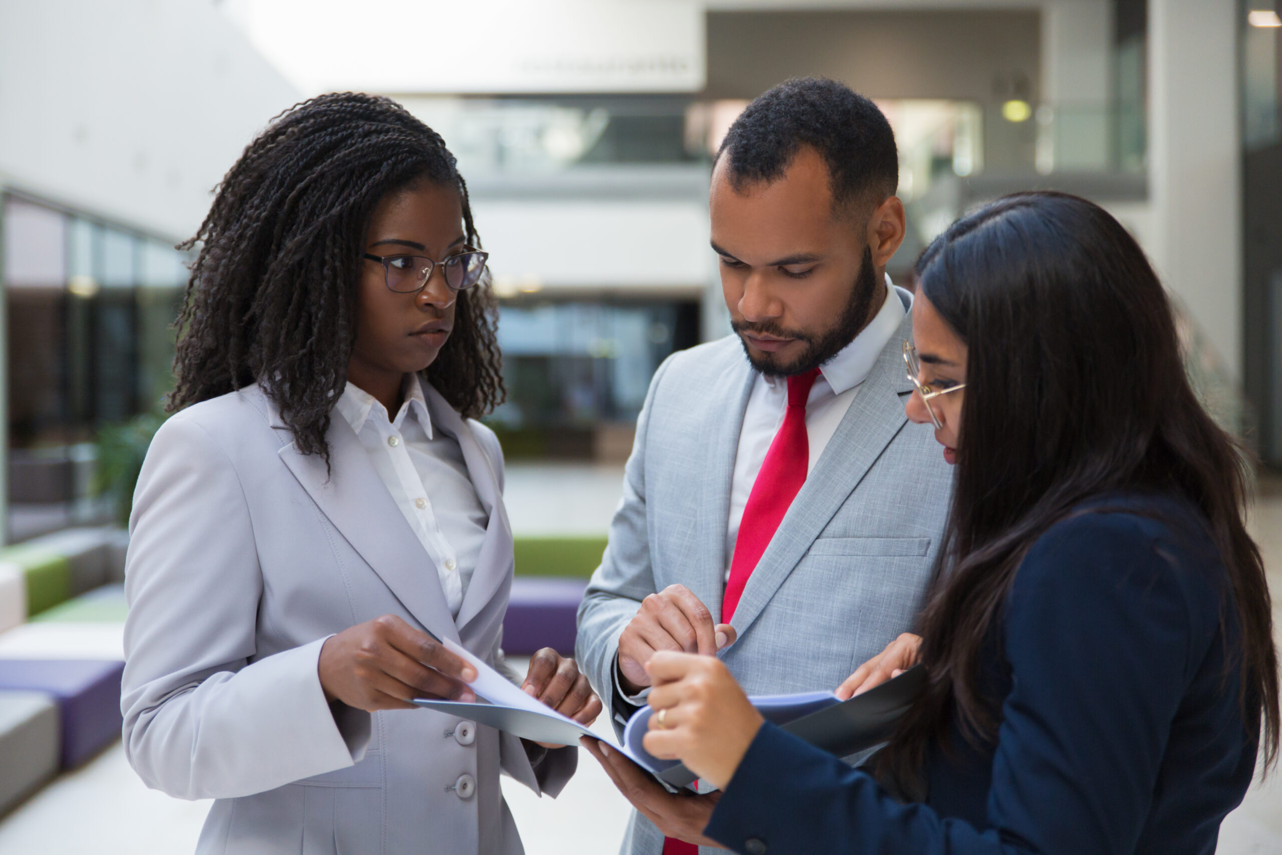 Serious coworkers discussing papers. Focused multiethnic young business colleagues standing together and looking at folder with documents. Business concept